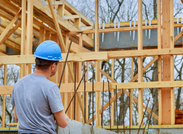 Stock image of a contractor looking at plans for a house that studs are being set up.